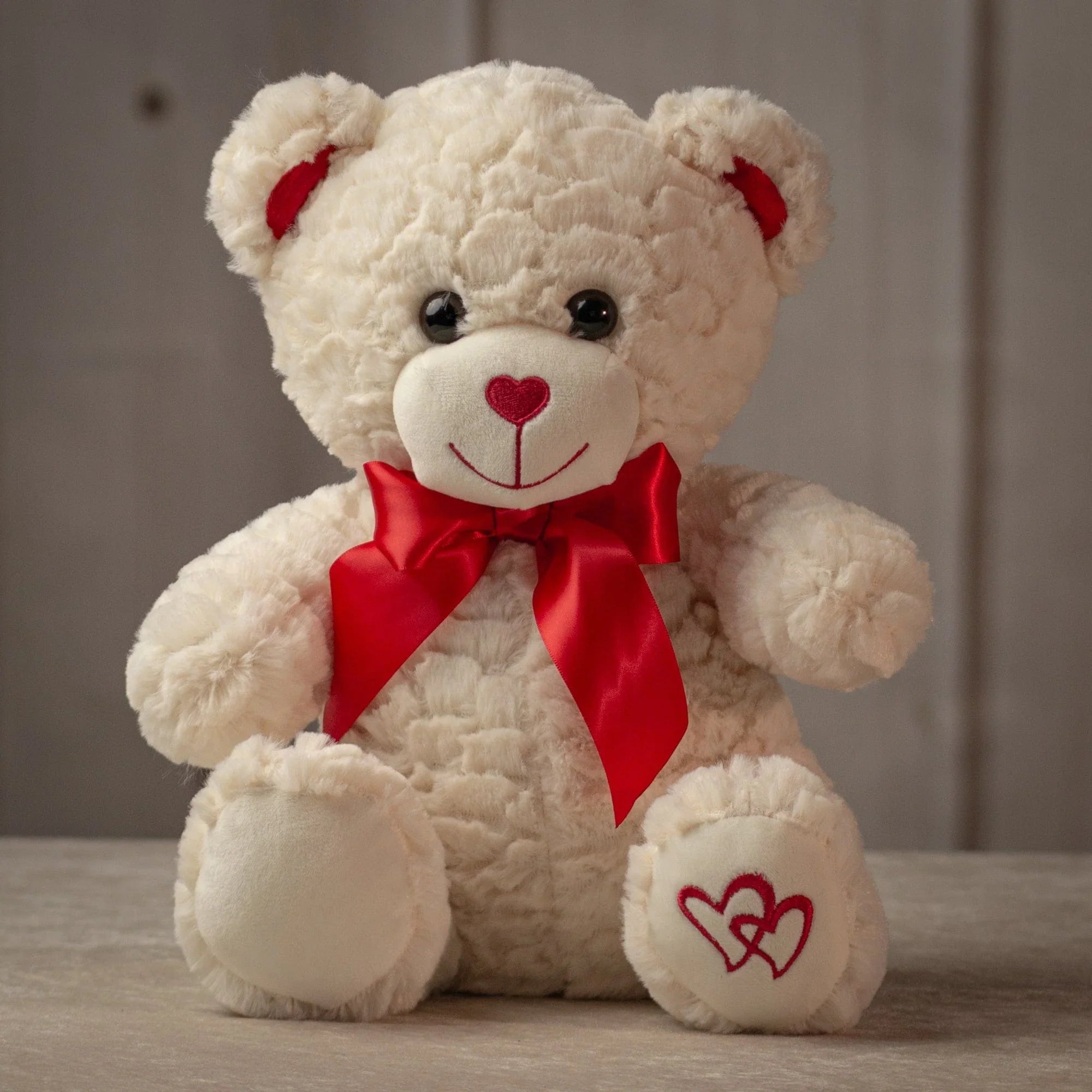 Adorable colored teddy bear with a red bow and heart details on its foot, perfect for gifting