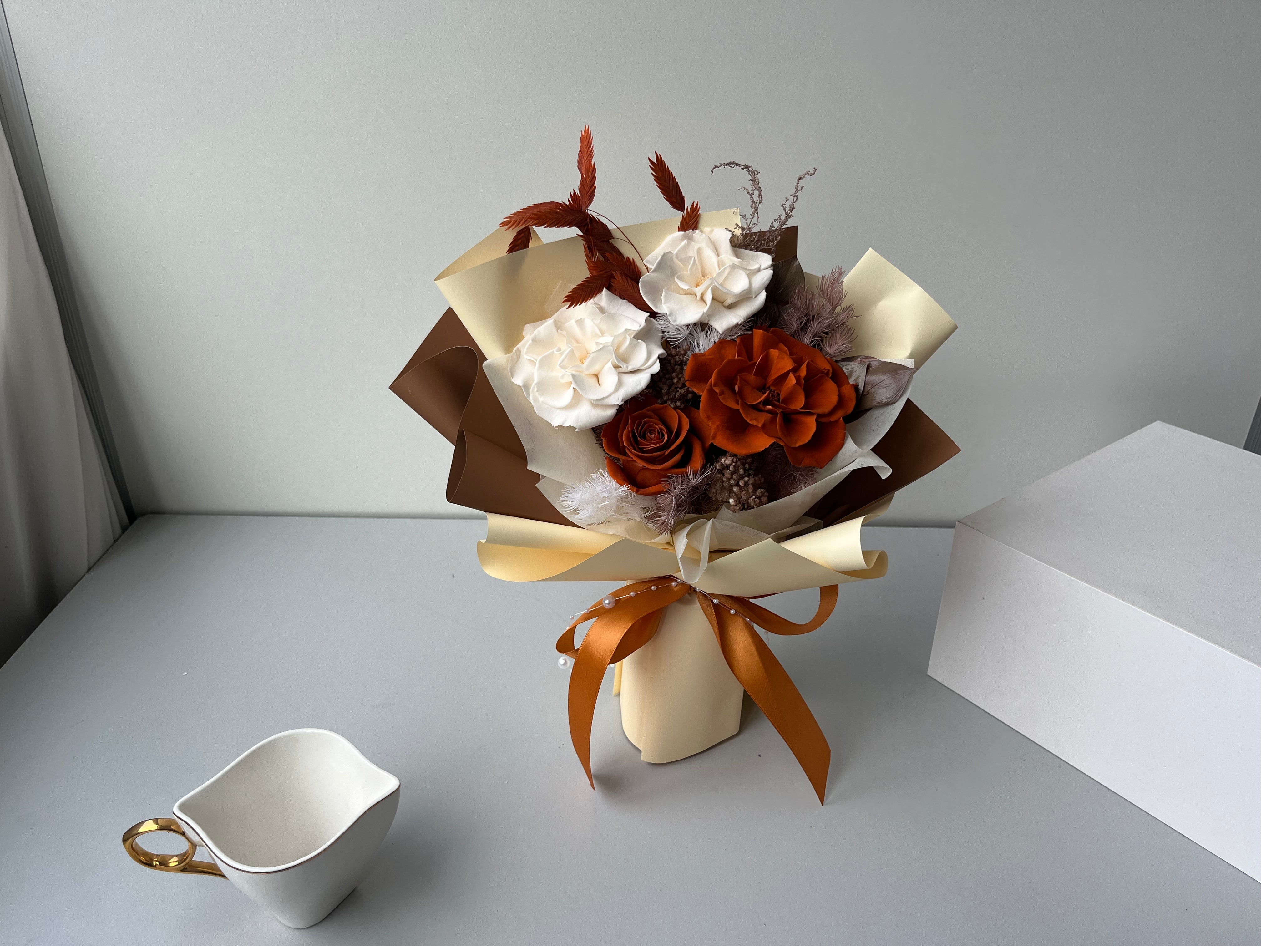 Elegant bouquet of white and orange roses arranged with autumnal accents and wrapped in warm tones.